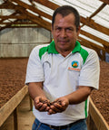 Lino Sinarahua Guerra, member of ACOPAGRO co-op in Peru holds drying cacao beans in his hands standing in front of raised drying beds