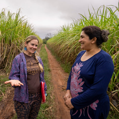 Equal Exchange's Laura Bechard visits with Manduvira sugar producer standing on a dirt road between two sugarcane fields