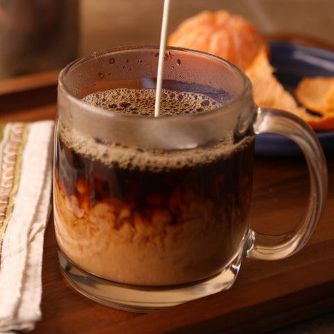 pouring cream into a glass mug of dark roast organic coffee