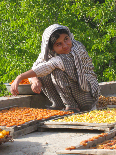 Farmer Ms Naheed sitting and smiling on patio while drying apricot and pineapples